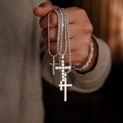 Silver diamond cross, plain cross and crucifix pendants hanging from hand