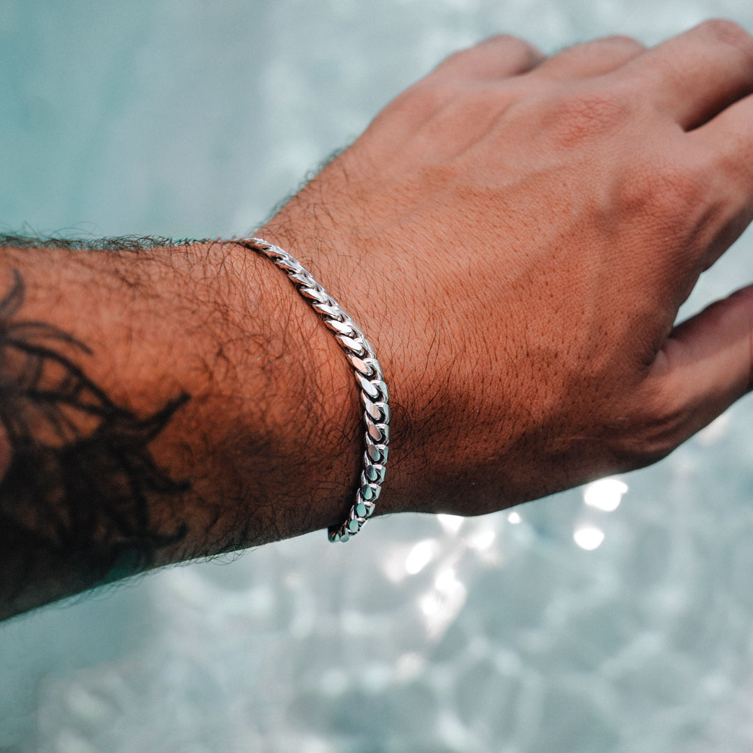 Hand with a silver cuban link bracelet against a water background