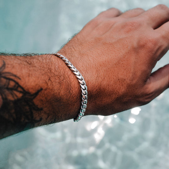 Hand with a silver cuban link bracelet against a water background
