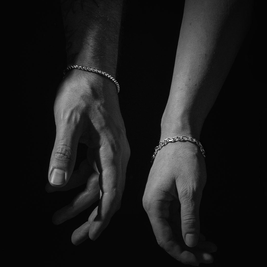 Black and white image of two hands with silver bracelets on a dark background