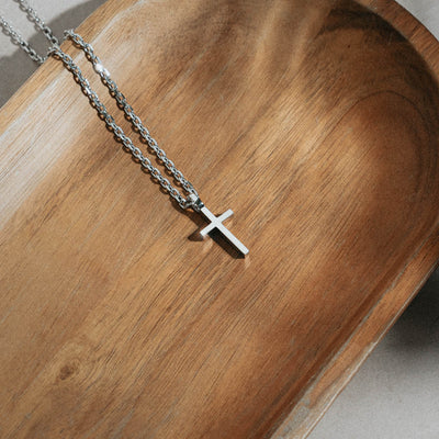 small cross pendant with silver necklace on wood tray
