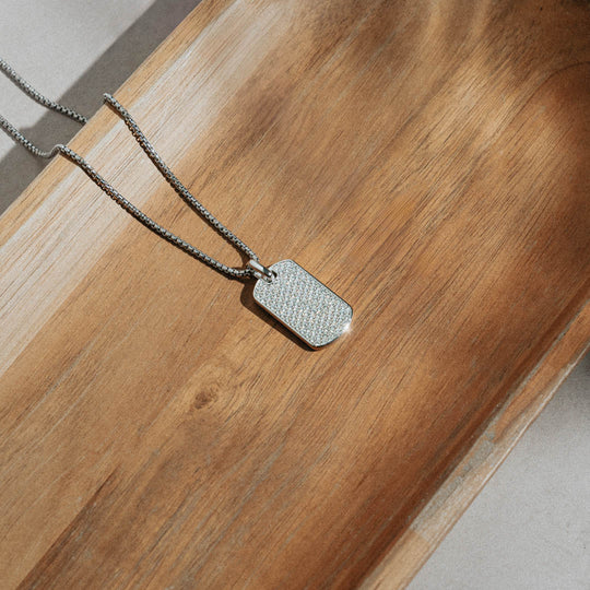 diamond dog tag pendant on silver necklace in a wooden tray